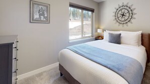 A bedroom with a bed, a window, a wall decoration, and a nightstand. - Beautiful Echo Landing Retreat, Sleeps 8, 3 Bdrm, Private Hot Tub, Ski In/Out  (Sun Peaks)