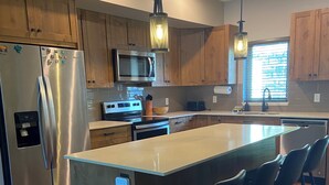 A modern kitchen with wooden cabinets, stainless steel appliances, and a central island with bar stools. - Beautiful Echo Landing Retreat, Sleeps 8, 3 Bdrm, Private Hot Tub, Ski In/Out  (Sun Peaks)