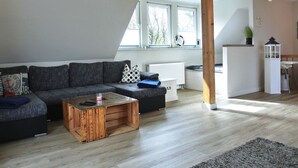 A modern living room with a sectional sofa, a wooden coffee table, and a view of the outdoors through large windows. - Vacation home directly on the dune, approx. 50 m to the Baltic Sea - Markgrafenheide (Rostock)