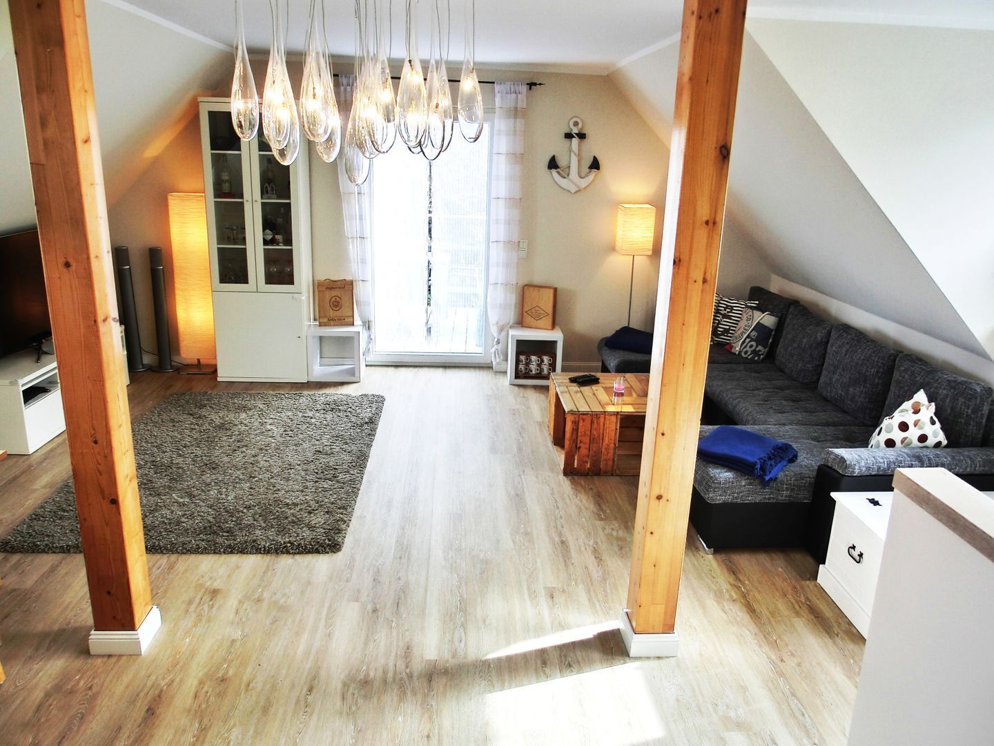Amplio loft con techo alto, vigas de madera a la vista, un gran ventanal, una zona de estar acogedora con sofá y sillones, y una mesa de comedor.