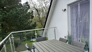 A deck with a table and chairs, overlooking a garden and a white building. - Vacation home directly on the dune, approx. 50 m to the Baltic Sea - Markgrafenheide (Rostock)