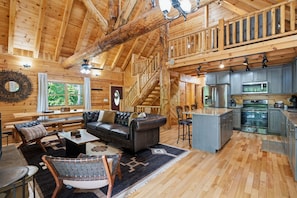 A log cabin interior with a living area, kitchen, and staircase.