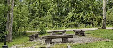 A picnic area with benches and a stone structure, surrounded by trees and greenery.