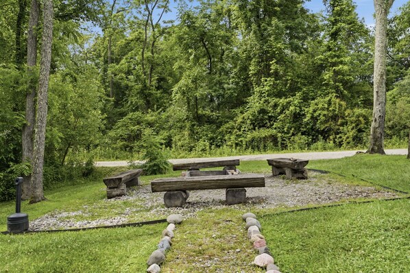 A picnic area with benches and a stone structure, surrounded by trees and greenery.