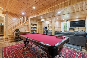 A wooden interior with a pool table, sofa, and staircase.