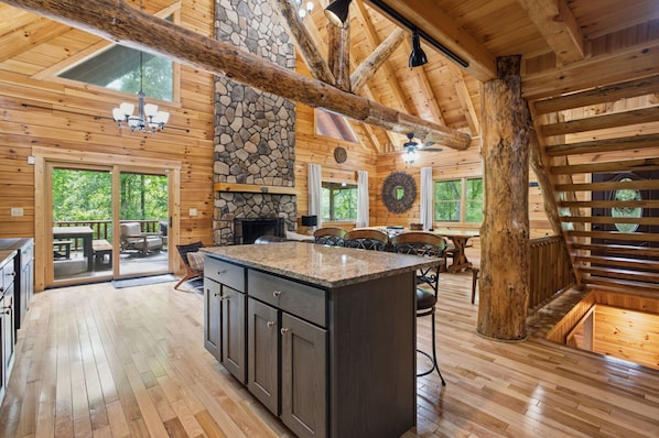 A spacious wooden cabin interior with a stone fireplace, large windows, and a dining area.