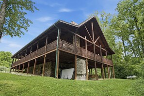 Una gran estructura de madera con varios balcones y cimientos de piedra, rodeada de vegetación.