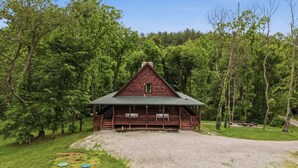 A wooden cabin with a porch, surrounded by dense forest.