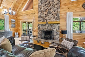 A log cabin interior with a stone fireplace, leather furniture, and a view of the outdoors.