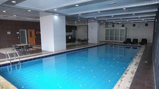 An indoor swimming pool with clear water, surrounded by a tiled deck and a few lounge chairs. - Lujosa Suite Privada: Cama King y Piscina en Lugar Céntrico y Seguro (Quito)