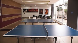 A room with ping pong tables, a large window with a view of palm trees, and artwork on the walls. - Lujosa Suite Privada: Cama King y Piscina en Lugar Céntrico y Seguro (Quito)