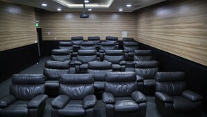 A cinema room with rows of leather recliner seats, wooden panel walls, and a ceiling-mounted projector. - Lujosa Suite Privada: Cama King y Piscina en Lugar Céntrico y Seguro (Quito)