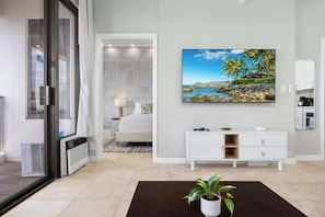 Quarto de hotel moderno com uma cama, cômoda branca, pintura de uma praia e um vaso com planta.