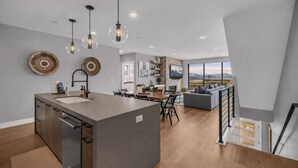 Une cuisine moderne dotée d’un îlot central, de luminaires suspendus et d’un coin repas offrant une vue sur l’extérieur.