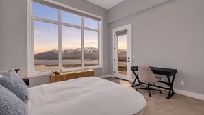 Une chambre avec une grande fenêtre, un lit, un bureau et une vue sur les montagnes et un lac.