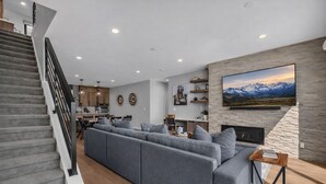 Un salon moderne avec un grand canapé d’angle gris, une cheminée et un grand téléviseur fixé au mur.