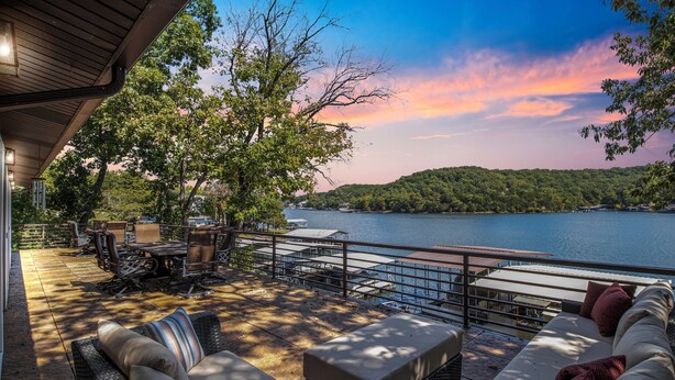 Eine Terrassensitzgruppe im Freien mit Blick auf einen See, ausgestattet mit Sofas und einem Esstisch.