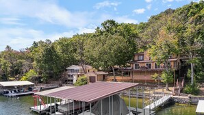 Ein an einem Steg liegendes Boot, ein kleines Haus mit Balkon und ein größeres Haus mit Terrasse.
