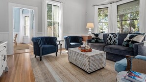 Ein Wohnzimmer mit blauem Sessel, grauem Sofa und Couchtisch mit Muster.