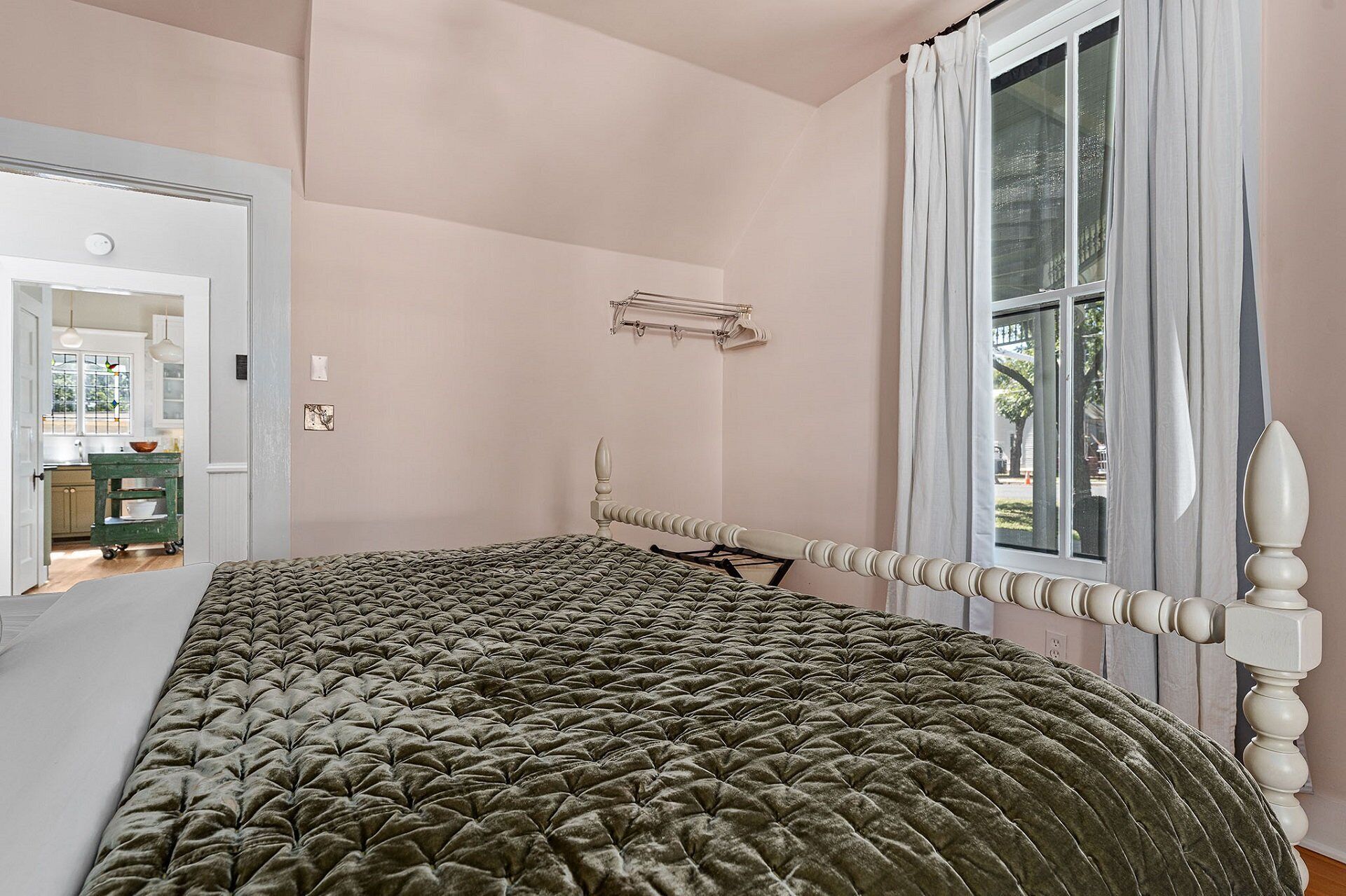 Ein Schlafzimmer mit einem großen Bett, einem Fenster mit Vorhängen, einem Holz-Kopfteil und Blick nach draußen.