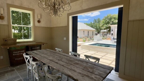 Ein Holzespeisesaal mit Stühlen, einer Chandelieber, einem Fenster mit Blick auf Bäume und einer Tür, die zu einer Terrasse mit Pool führt.