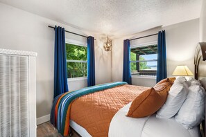 A bedroom with a bed, curtains, a window, a lamp, and a view of the outdoors.