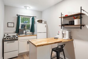 Cozinha compacta com fogão, micro-ondas, geladeira e uma mesa de madeira.