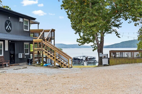 Un bâtiment avec un escalier menant à une terrasse d’où l’on a vue sur une étendue d’eau, un panneau indiquant une zone d’accès aux bateaux, et un arbre au premier plan.
