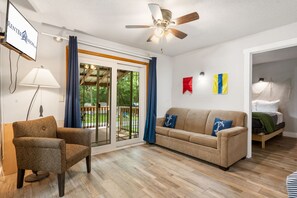 Un salon comprenant un canapé, un fauteuil, un ventilateur de plafond et une porte-fenêtre coulissante donnant sur un espace extérieur.