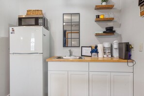 Une cuisine compacte équipée d’un réfrigérateur, d’un four à micro-ondes, d’un évier et de divers appareils électroménagers.