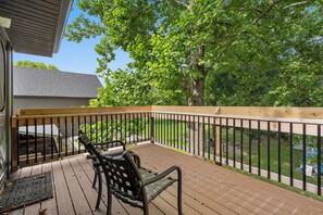 A wooden deck with a metal railing, a bench, and a view of a backyard with trees and a lawn.