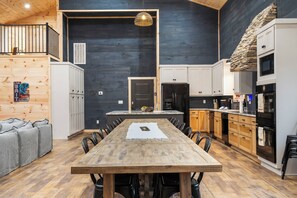 A modern kitchen with a large dining table, wooden cabinets, and a stone accent wall.