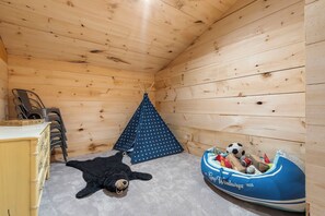 A cozy cabin interior with a sleeping area, a small tent, a boat-shaped bed, and a bear plush toy.