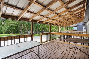 Une terrasse extérieure couverte, dotée de bancs et de tables en bois, et entourée d’arbres.