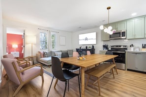 A modern kitchen with a dining area, wooden flooring, and a large window.