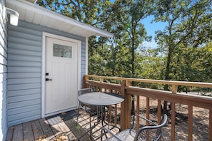 A small wooden deck with a metal table and chairs, a door with a window, and a railing.