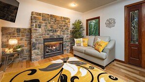 A cozy living room with a stone fireplace, a sofa with yellow cushions, and a decorative rug. - Horseshoe Acres - Home theater, spa room, hot tub (Oak Hill)