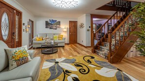A living room with a staircase, wooden flooring, a floral rug, and a sofa with decorative pillows. - Horseshoe Acres - Home theater, spa room, hot tub (Oak Hill)