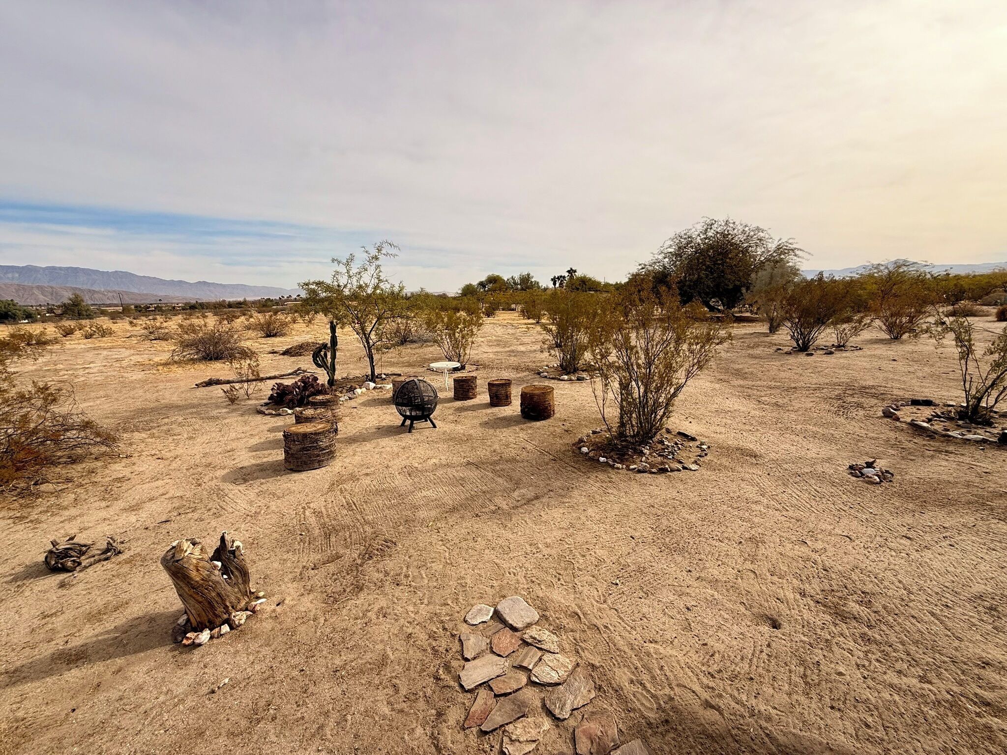 A desert landscape with sparse vegetation, a few small structures, and a distant mountain range.