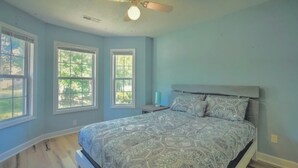 Un dormitorio con una cama, dos ventanas, un ventilador de techo y una mesita de noche.