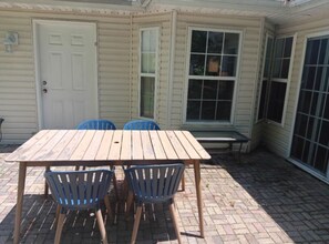 Une table en bois, accompagnée de quatre chaises, se trouve dans un patio abrité dont le sol est recouvert de briques.
