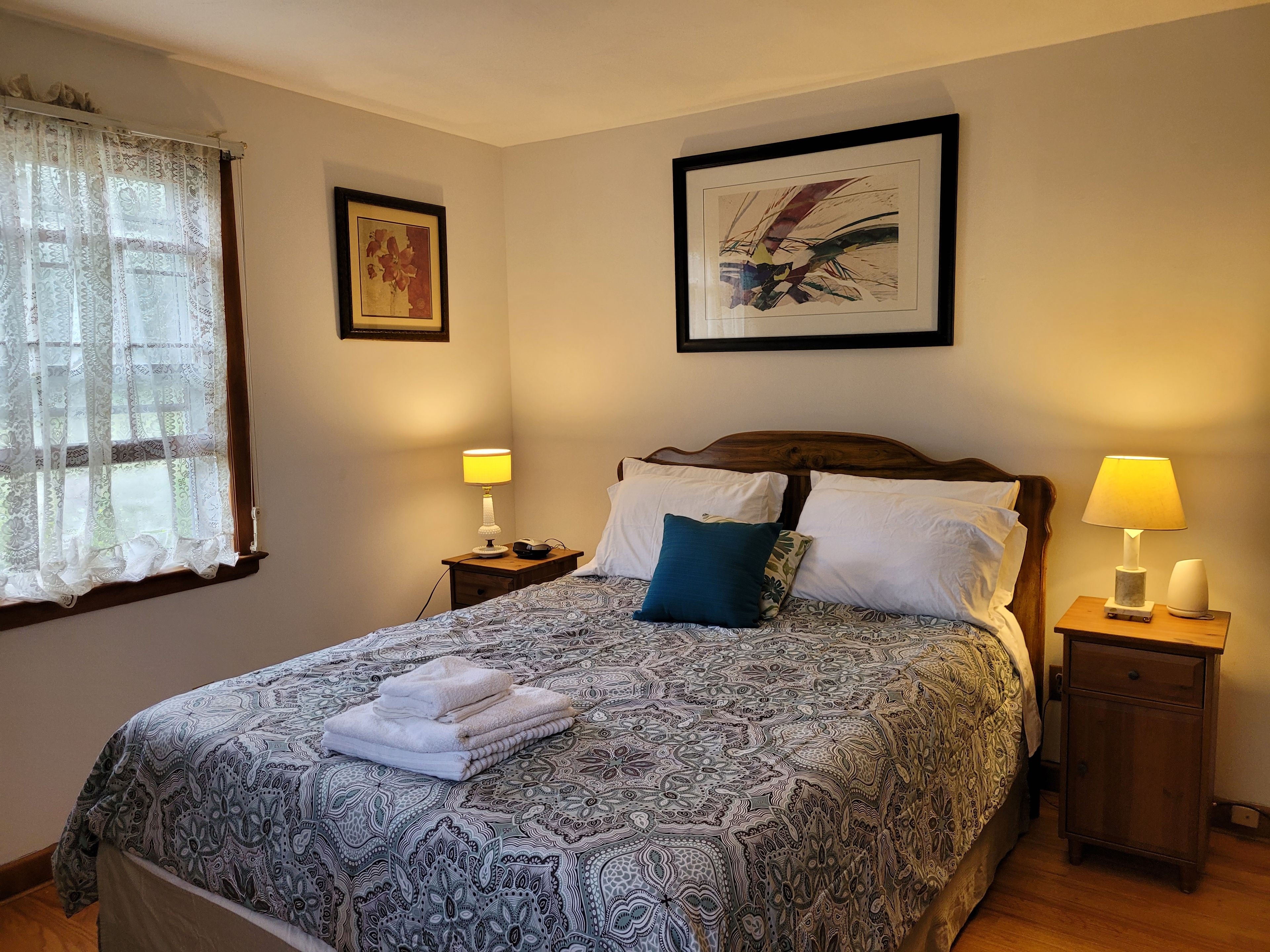 A neatly made bed with patterned bedding, two bedside lamps, and a framed abstract painting on the wall.