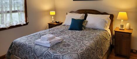 A neatly made bed with patterned bedding, two bedside lamps, and a framed abstract painting on the wall.