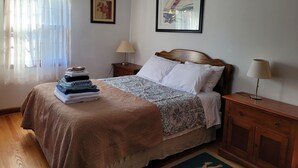 Un lit bien fait, recouvert d’une couvre-lit à motifs, une pile de serviettes pliées et deux lampes de chevet posées sur des tables de nuit en bois.