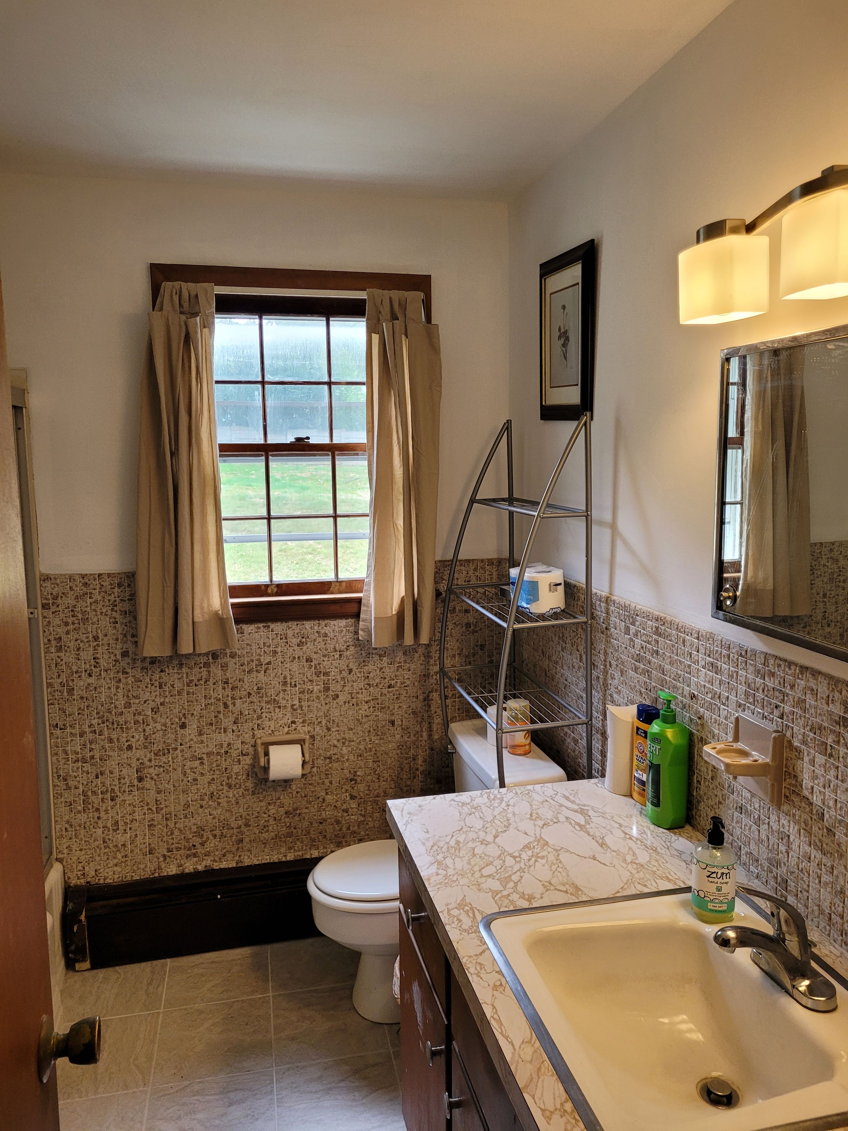A bathroom with a toilet, sink, and window with curtains.