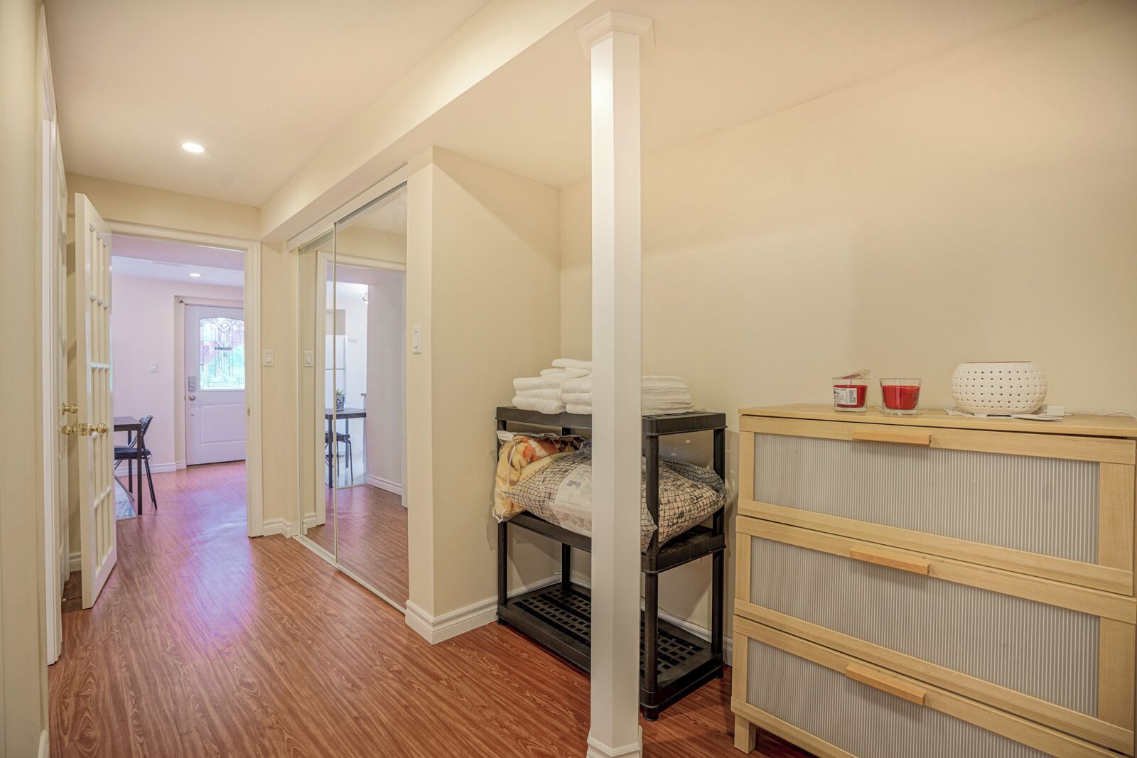 Un couloir doté d’un plancher en bois, une porte en verre donnant sur un coin repas, et un lit avec une tête de lit et des oreillers.