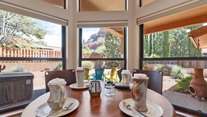 A dining table with plates, cutlery, and a pitcher, set against a backdrop of a scenic outdoor view through large windows. - Sedona Among the Rocks: Luxurious 3BR home with stunning Red Rock views in the Chapel Area. (Sedona)