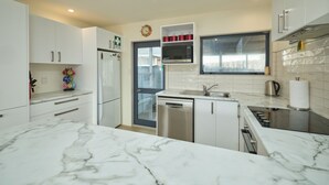 A modern kitchen with white cabinets, a stainless steel refrigerator, a microwave, and a dishwasher. - Handy Location | Ocean & Mountain Views | Spacious Yard - KK46451 (Kaikoura)