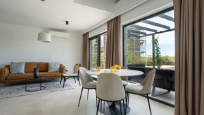 A modern living room with a sofa, a dining table with chairs, and large windows offering a view of the outdoors. - Stunning home in Bale (Bale)
