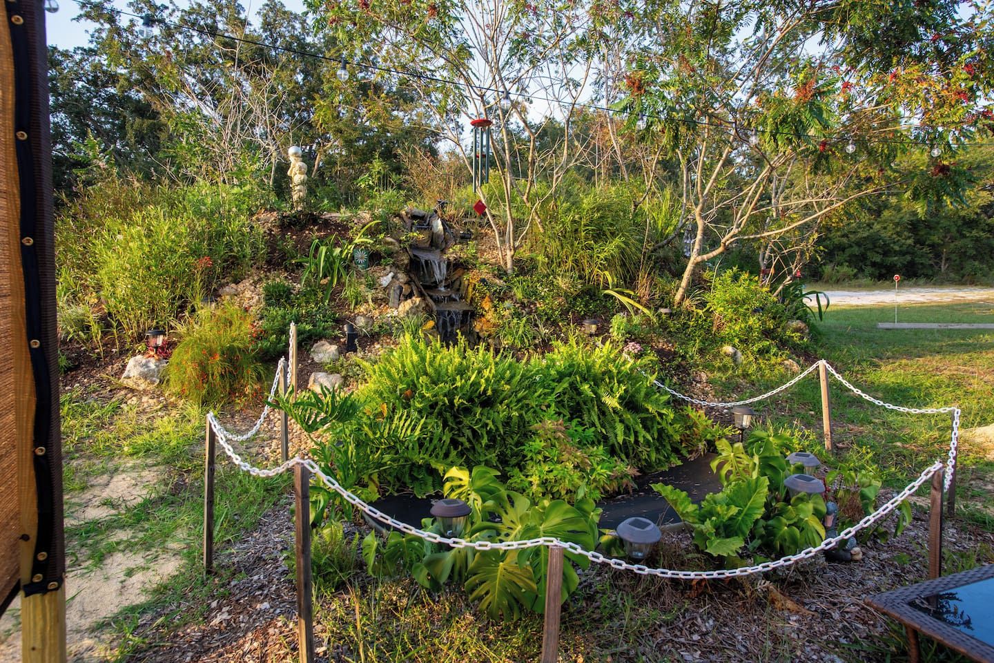 A garden with a water feature, chain-link fence, and various plants.
